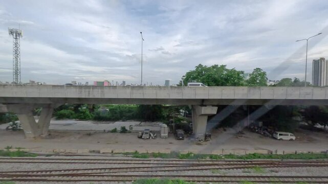 view from the window of an SRT Red Line train in Bangkok, Thailand. The passing scenery includes various urban elements such as residential buildings, commercial structures, other railway tracks