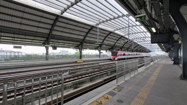 Bang Khen Station, part of the SRT Red Line suburban railway system in Bangkok, Thailand. A modern electric train is visible, either arriving and departing from the elevated station platform.