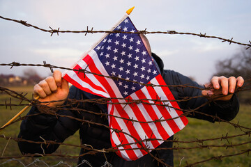Concept of United States of America closed borders. Sad man at barbed fence., holding USA flag