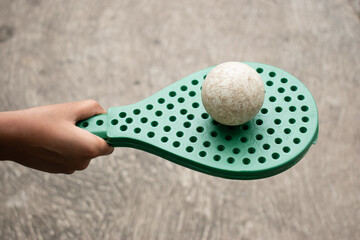 A close-up of a hand holding a green perforated paddle with a ball balanced on top, showcasing focus and coordination in a simple yet engaging play moment.