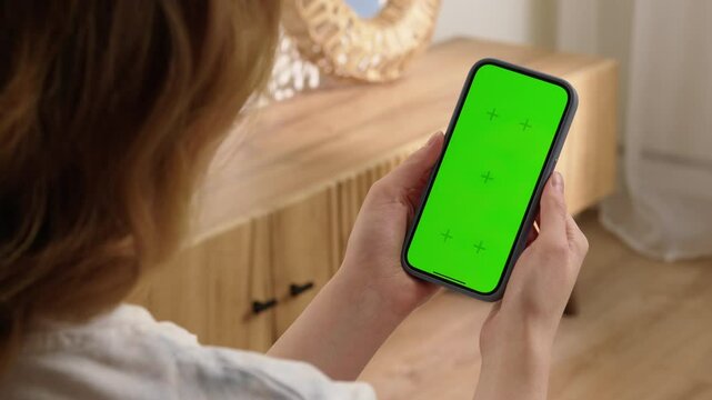 Woman use digital tech cell phone open green screen mock up. Hand press click phone web site middle center. Girl hold mobile. Turn on chroma key page. Cozy home background. Online app copy space.