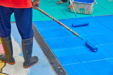 Low section of  worker using paint roller and painting blue color on the road