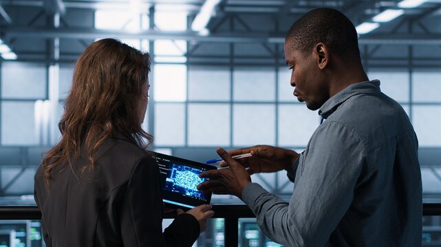 Data center system administrators using artificial intelligence neural networks tech on tablet. Teamworking server farm employees using AI programming language on device screen, camera A