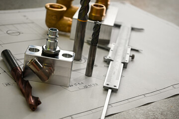 Metal drill bits, end mill, caliper and plumbing connectors lying on a technical drawing,...