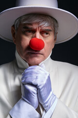 Close-up portrait of sad clown. An elderly man in a white coat and hat.