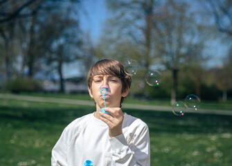 Caucasian male child blowing bubbles in sunny park