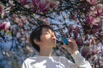 Young caucasian male blowing bubbles under blooming magnolia tree