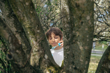Caucasian young boy blowing bubbles outdoors among trees