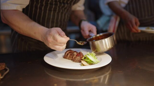 View of a chefs hand pouring sauce over a perfectly cooked piece of meat as he plates up a meal in a fine dining restaurant