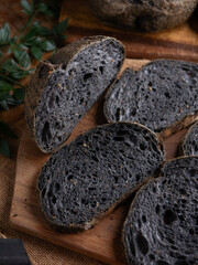 Fresh baked black charcoal sourdough ciabatta bread sliced on wooden board.