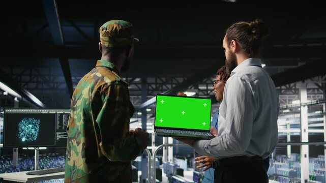 Army tech specialist in data center and coworkers using green screen laptop to troubleshoot military computer systems. Soldier and command center server room admins using chroma key notebook, camera A