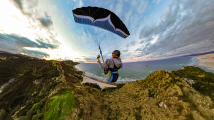 Extreme paragliding pilot soaring in the New Zealand beach at sunset. Adventure concept