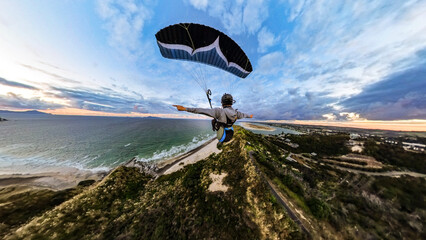 Extreme paragliding pilot soaring in the New Zealand beach at sunset. Adventure concept