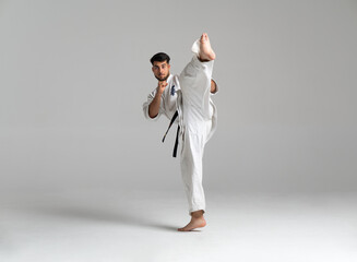 Kyokushinkai karate fighter kicking high in grey background