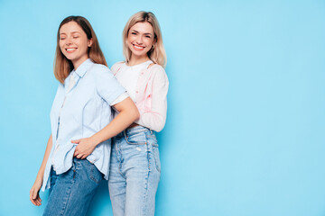 Fototapeta premium Two young beautiful smiling brunette hipster female in trendy summer clothes. Lovely women posing on blue background in studio. Positive models having fun. Cheerful and happy. isolated