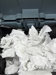 This image shows an overhead view inside a trash can. The can is lined with a black trash bag and is filled with crumpled white paper towels.