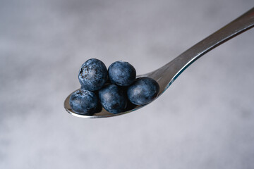 Close-up of fresh blueberries on metal spoon with grey background