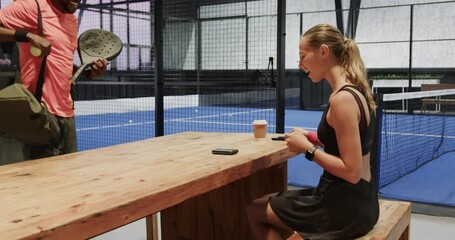 Diverse athletes preparing for padel tennis match, checking smartphones at indoor court - Powered by Adobe