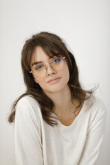 Obraz premium Stylish Young Woman In Glasses Wearing Casual White Top Against Neutral