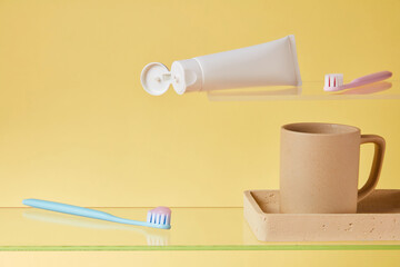 Pastel toothbrush in a mug next to a standing toothpaste tube on yellow floor with green background. Minimalist vibe for clean lifestyle and health visuals.