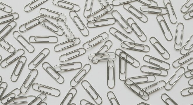 Scattered metal paperclips on a white surface - Powered by Adobe
