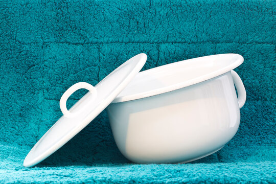 Nocturia concept. White chamber pot made from enamel on turquoise bath mat for collecting urine at night