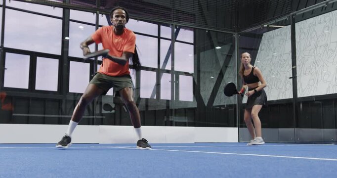 Man and woman playing padel tennis on indoor court, enjoying competitive match