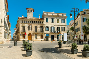 Historic architecture under a blue sky on a small town square in Mahon, Spain.
