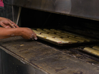 A baker's hands carefully place a tray of golden-brown, sesame-seed topped rolls into a commercial oven