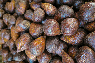 A close-up photo of a group of salak fruit or snake fruit from a traditional market, with their brown textured skin. Close Up of Salak Fruits texture material background.