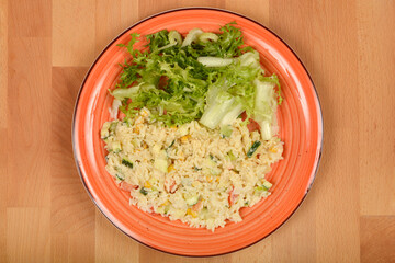 A colorful plate features a serving of vegetable risotto next to a fresh green salad on a wooden background