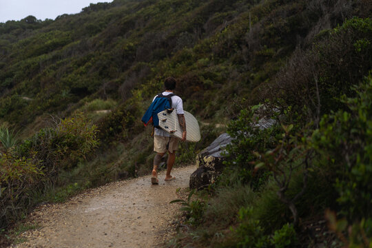 Young man carrying surfboard and walking to beach