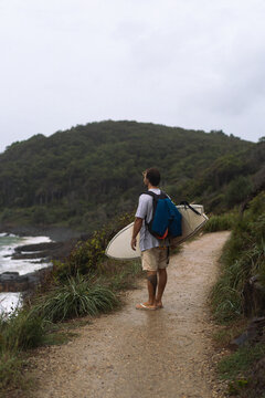 Young man carrying surfboard and walking to beach