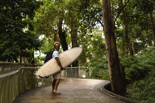 A middle aged man walks towards the beach with a surfboard
