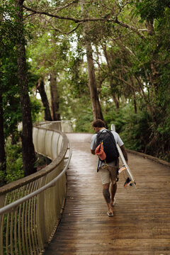 A middle aged man walks towards the beach with a surfboard
