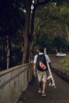 A middle aged man walks towards the beach with a surfboard