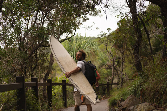Young man carrying surfboard and walking to beach