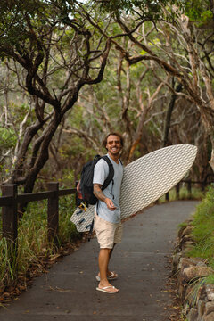 A middle aged man walks towards the beach with a surfboard