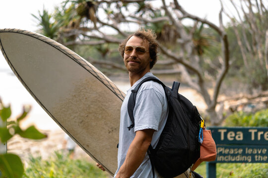 A middle aged man walks towards the beach with a surfboard