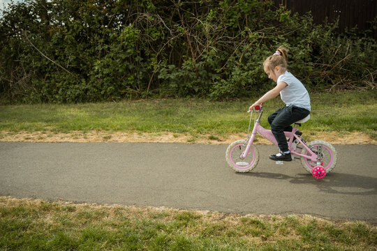 Little girl riding a pink bike in the park, copy space