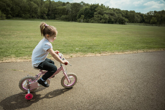 Little girl riding a pink bike in the park, copy space