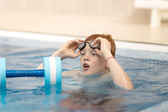 A young athlete adjusts his swimming goggles. Portrait of a swimmer putting on his goggles in the swimming pool