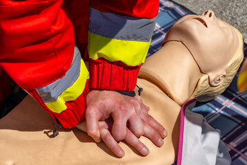 paramedic in a red and yellow reflective uniform performing chest compressions on a CPR training...