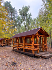 Wooden picnic gazebo in a park surrounded by greenery, offering shade and seating for outdoor...