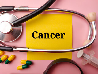 Sticky note and doctor's equipment with the word CANCER on a pink background