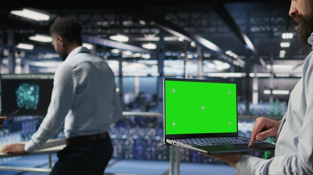 Close up of data center employee doing maintenance tasks on green screen laptop, ensuring optimal performance. Worker using mockup notebook to review diagnostics and apply patches, camera A
