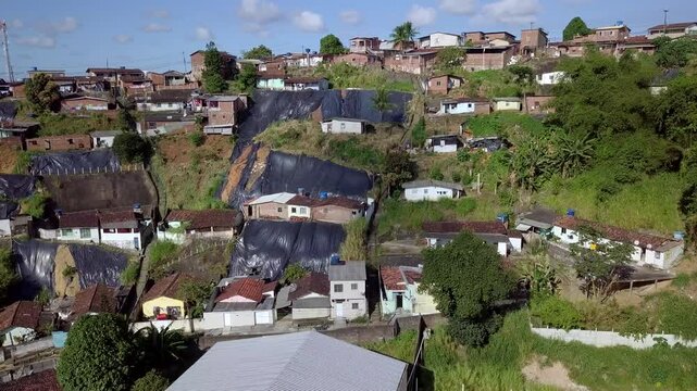 Aerial perspective over the Macaxeira neighborhood hillside in Recife Brazil focusing on the modest dwellings parked cars and protective tarps highlighting the pervasive poverty danger and inequality