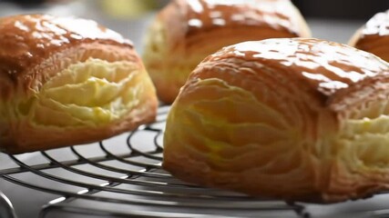 Cinematic close-up of golden puff pastry buns on cooling rack, slow orbit and zoom, flaky textures, warm kitchen mood - Powered by Adobe