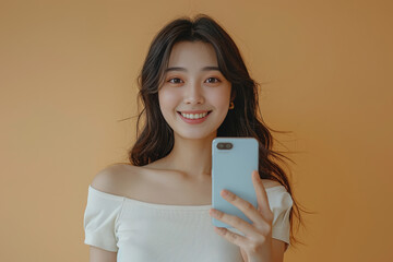 Naklejka premium Little girl holding up a smartphone and smiling brightly in a white dress on beige background.