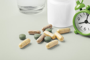 Natural supplement pills, vitamin capsule with medical bottle, alarm clock and glass of water on...
